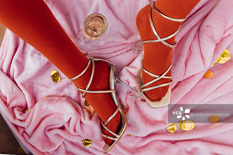 高跟凉鞋和红色紧身衣的俯视图，粉红色天鹅绒背景上有一杯香槟图片素材