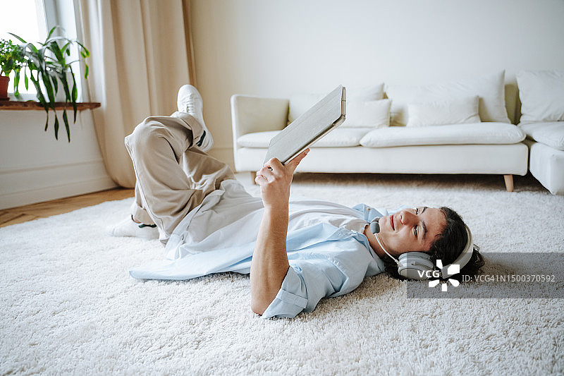 男孩躺在家里的地毯上玩平板电脑图片素材