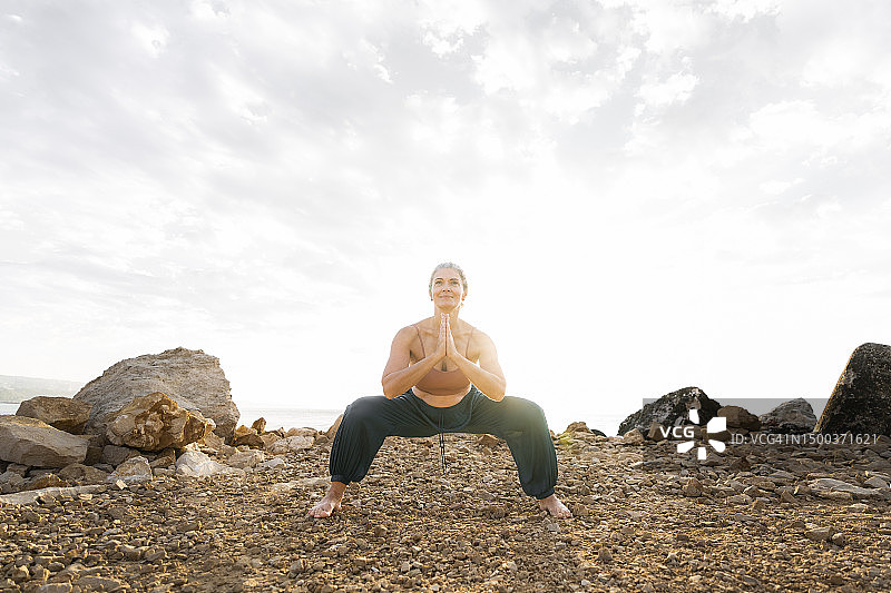 一名女子在海滩用蹲姿练习瑜伽图片素材
