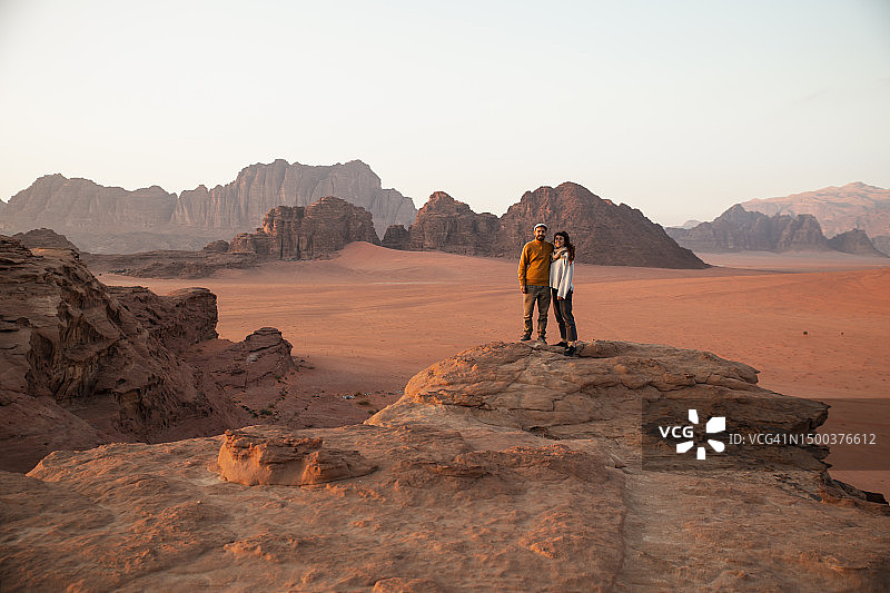 日落时分，一对夫妇站在沙漠的岩石上图片素材