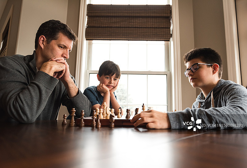 父子俩在桌旁下棋，小弟弟在旁边看着图片素材