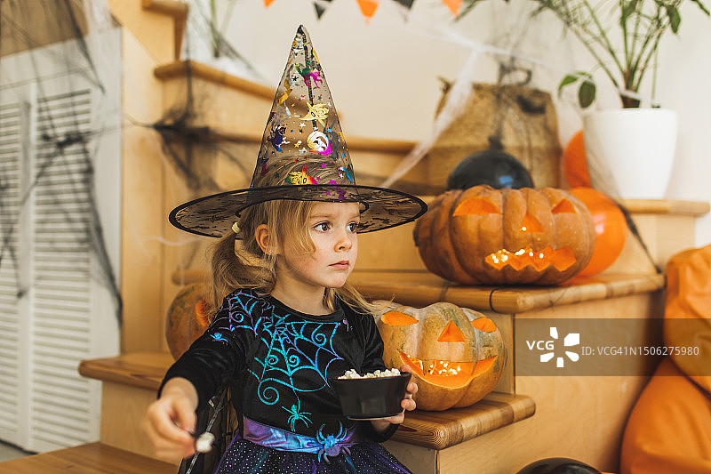 可爱的小女孩穿着女巫裙，戴着帽子，在孩子们的万圣节派对上吃爆米花图片素材