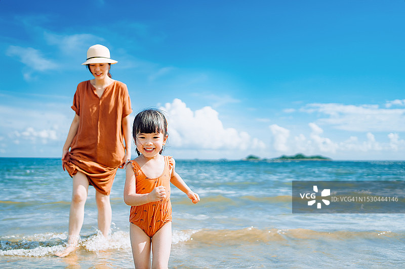 在一个阳光明媚的夏日，深情的年轻亚洲母亲和快乐的小女儿在海边散步，一起在大自然中玩耍，分享母女时光图片素材