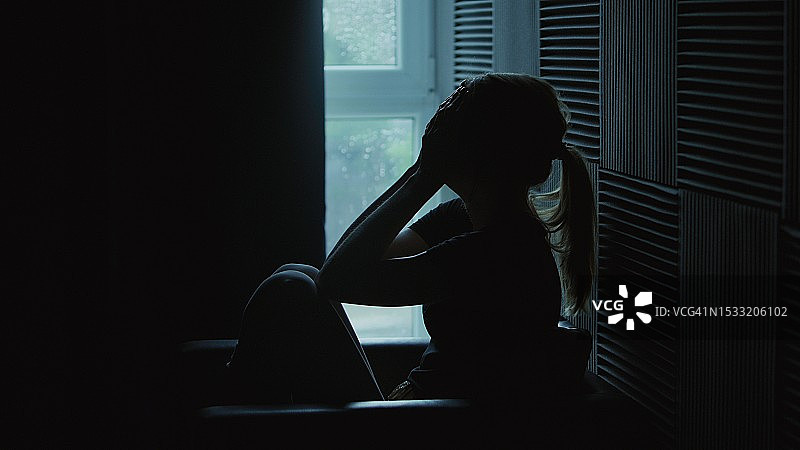 这个女孩坐在一个黑暗的房间里，精神崩溃——抑郁。图片素材