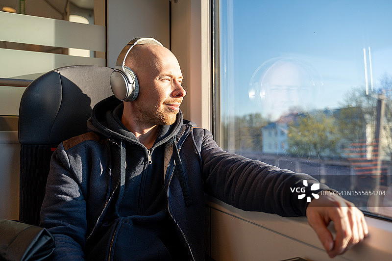 戴着耳机的秃头男人坐在行驶的火车上享受着，听着音乐图片素材
