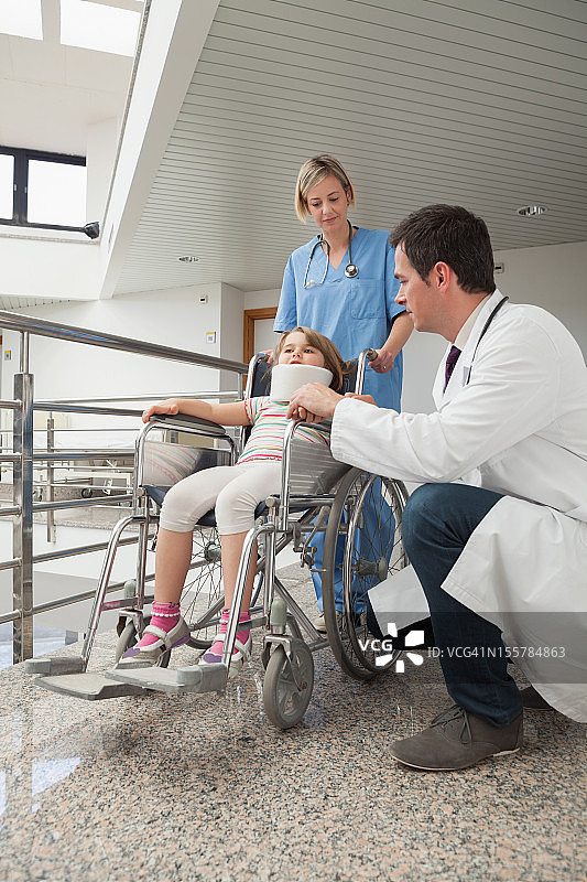 医生蹲在轮椅上的孩子旁边，护士推着轮椅图片素材