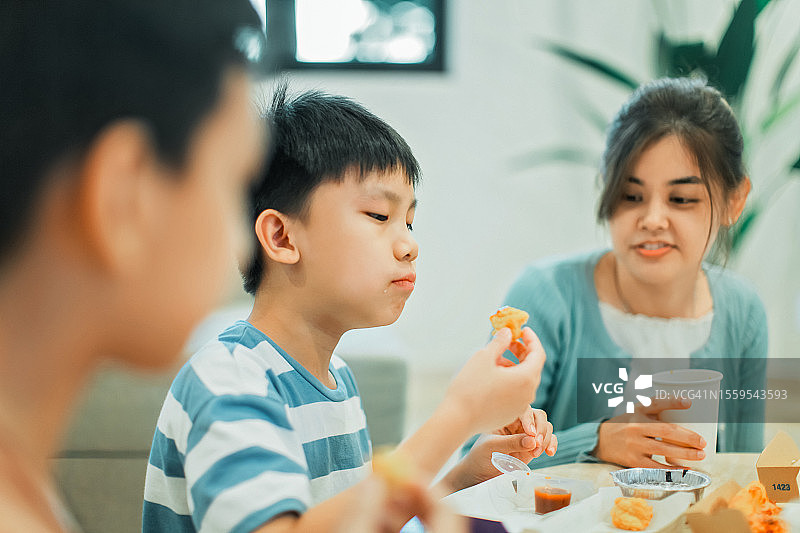 一个中国小男孩正在家里和家人一起吃鸡块。库存图片图片素材