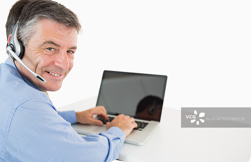 微笑的商人戴着耳机在笔记本电脑上工作图片素材