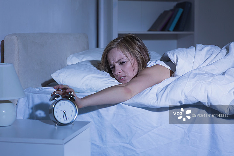 躺在床上的女人把手伸向闹钟图片素材