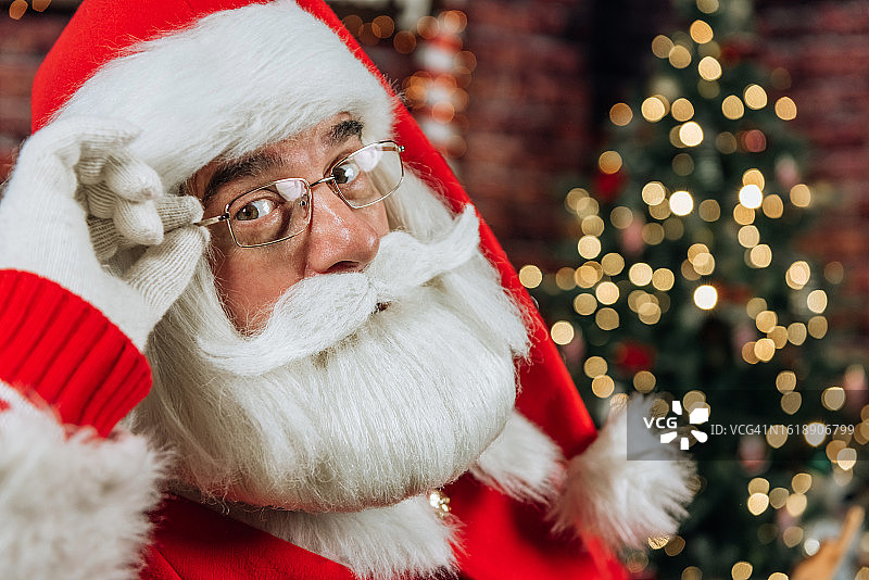 圣诞老人戴着眼镜的特写肖像，在一棵圣诞树的背景下看着相机图片素材