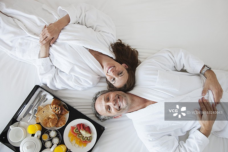 一对夫妇躺在床上，早餐放在一边图片素材