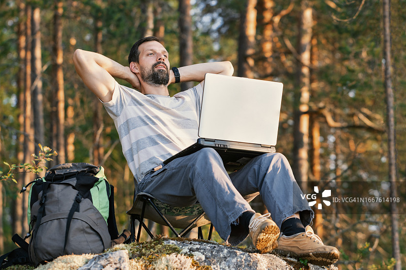 远程工作概念——人带着笔记本电脑在森林里享受，而背包旅行图片素材
