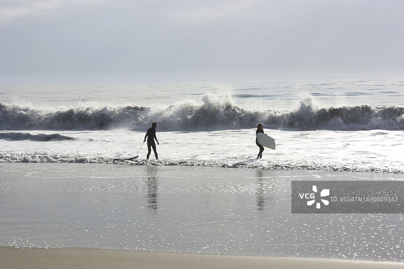 在美国加利福尼亚州阿普托斯的海崖州立海滩，两个人带着冲浪板走进太平洋图片素材