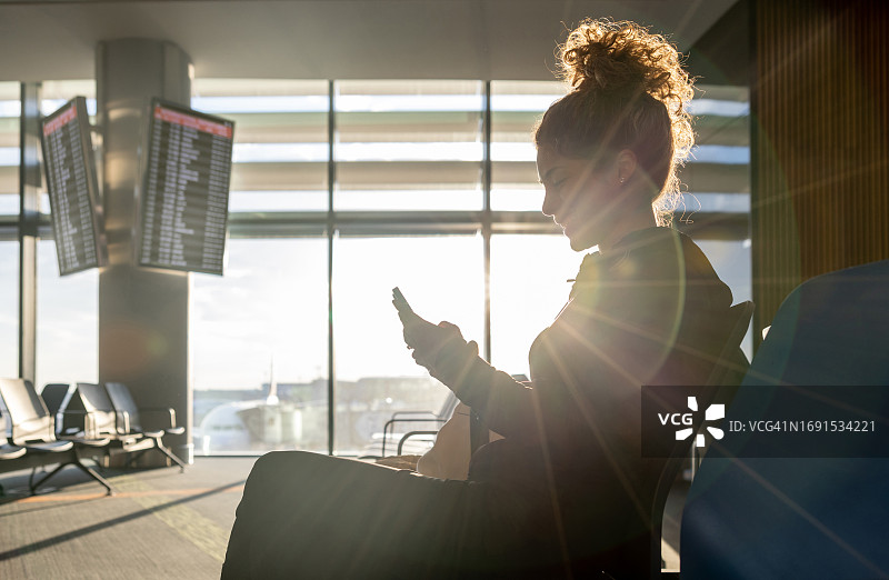女旅客在机场门口等候时用手机发短信图片素材