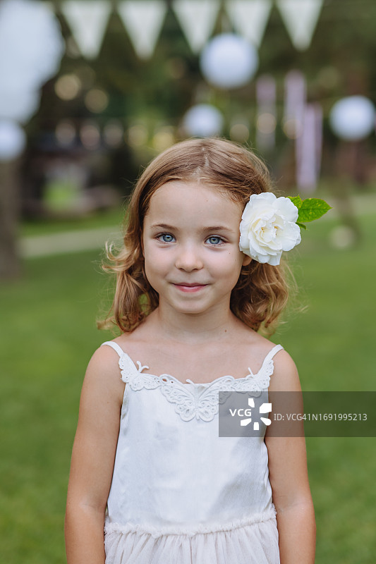 一个可爱的小女孩在花园聚会上，耳朵后面插着一朵白花。图片素材