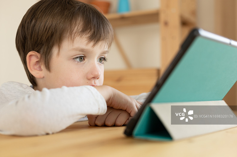 一个6岁的男孩正在家里用数码平板电脑学习图片素材