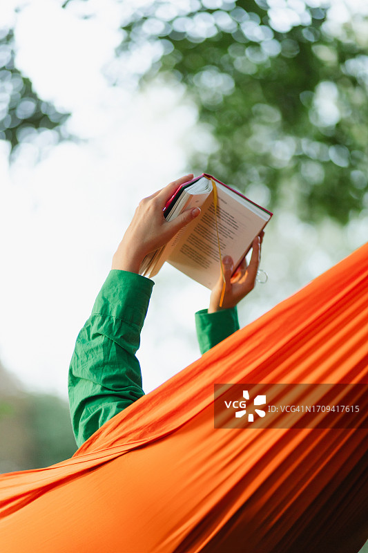 在公园的吊床上阅读时，一个女人的手拿着书的特写镜头图片素材