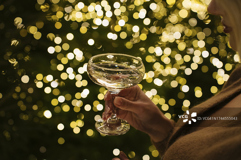 手持香槟酒杯的女子站在圣诞彩灯旁图片素材