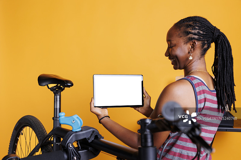 一名女子站在自行车旁使用数码平板电脑，背景是黄色图片素材