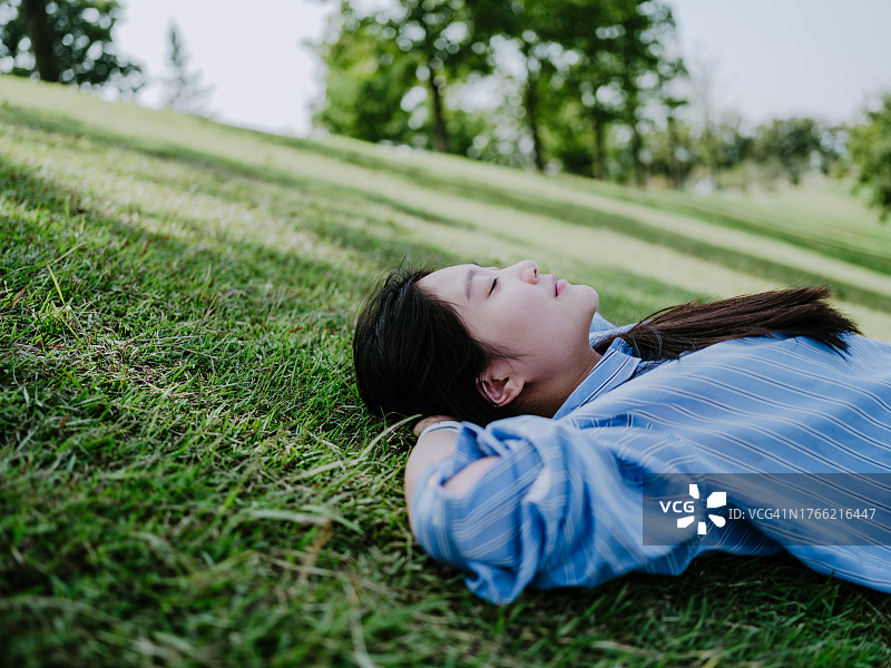 一个闭着眼睛躺在草地上的亚洲女人图片素材