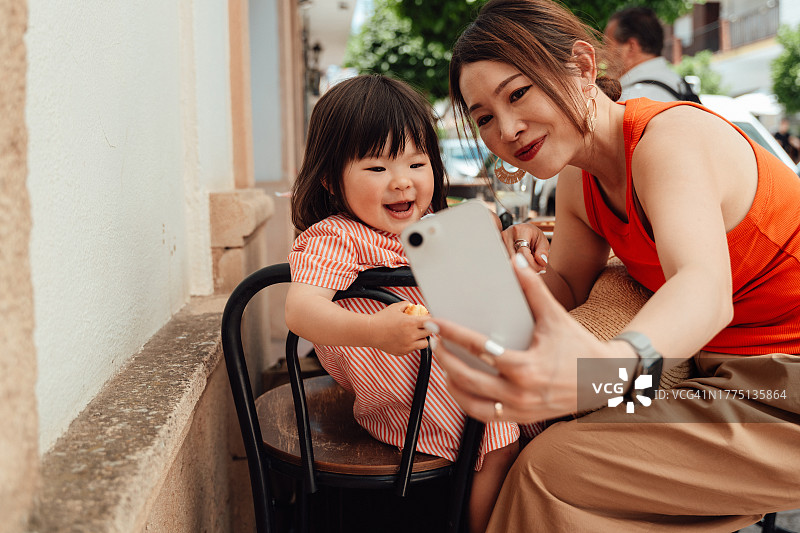 亚洲母亲和蹒跚学步的女儿用智能手机自拍，并在社交媒体上分享图片素材