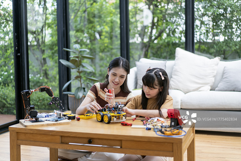 好奇的女儿和她的母亲看着他们制造的机器人汽车原型的蓝图图片素材