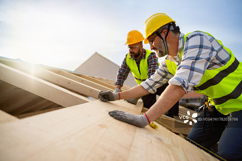 中年白人男性屋面工在制作屋梁时测量和标记木材的位置图片素材