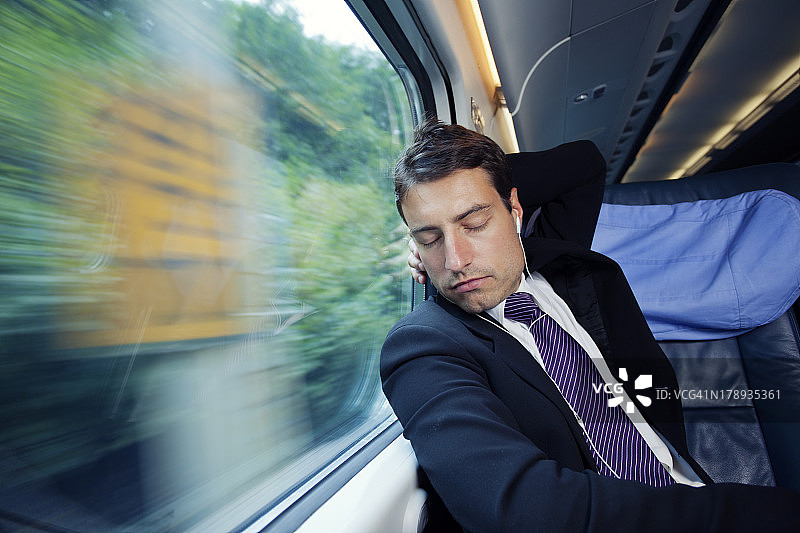 一个商人坐在火车上靠窗休息，边听音乐边休息图片素材