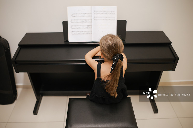 漂亮的小女孩在客厅弹钢琴。可爱的学龄前儿童在学习演奏乐器图片素材