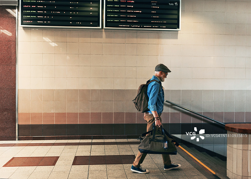 时髦的老人走过火车站，拿着行李袋回家。老人走进地铁站。图片素材