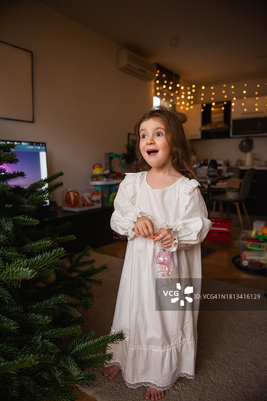 小女孩手里拿着粉红色水母形状的玻璃玩具，旁边是绿色的真圣诞树图片素材