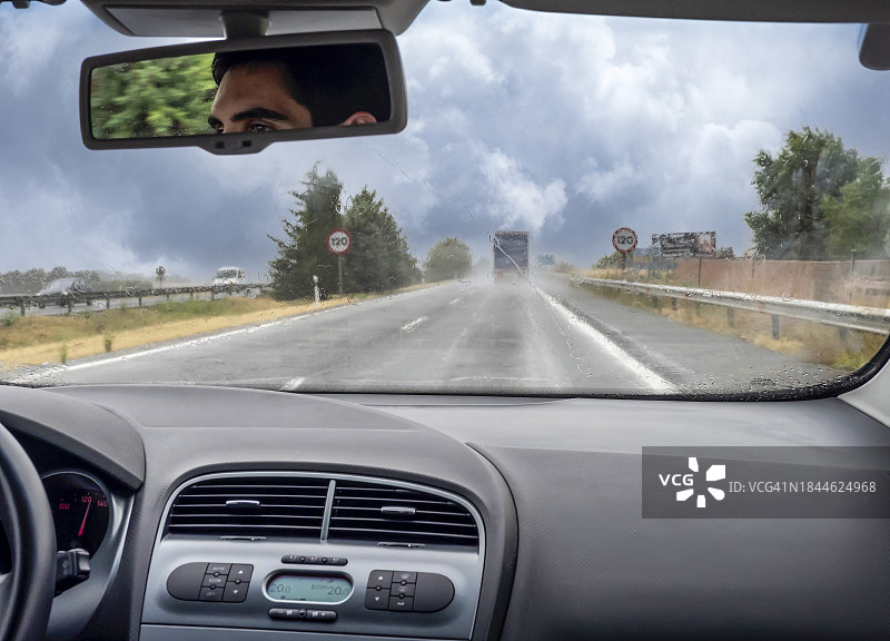 从汽车的角度来看，一个年轻人在一个狂风暴雨的日子里驾车行驶在高速公路上。图片素材