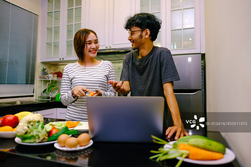 年轻的亚洲夫妇在一起做饭时使用笔记本电脑。图片素材