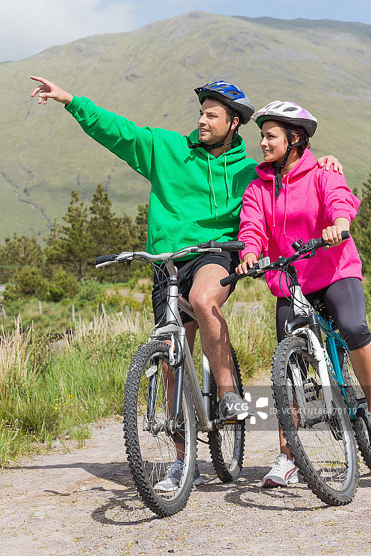运动夫妇骑自行车戴兜帽套头衫与男人指着图片素材