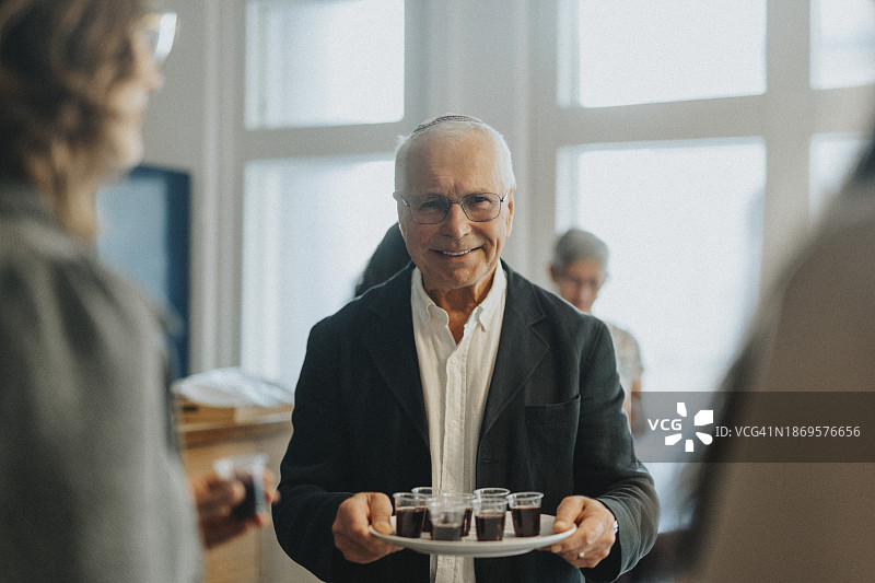 在犹太教堂举行的犹太集会上，微笑的老人拿着一盘酒杯的肖像图片素材