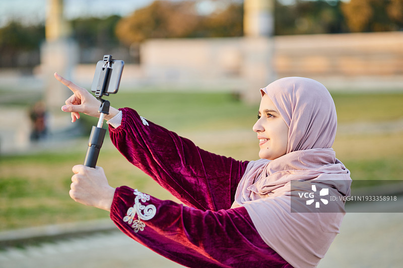 年轻的穆斯林妇女在街上用手机发视频。图片素材