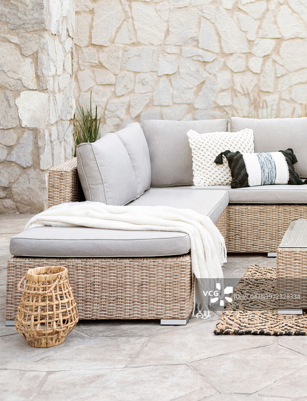 春季庭院家具与藤节沙发，装饰枕套，柳条庭院椅，藤咖啡桌，在一个室外生活空间的植物区域地毯，装饰石墙图片素材