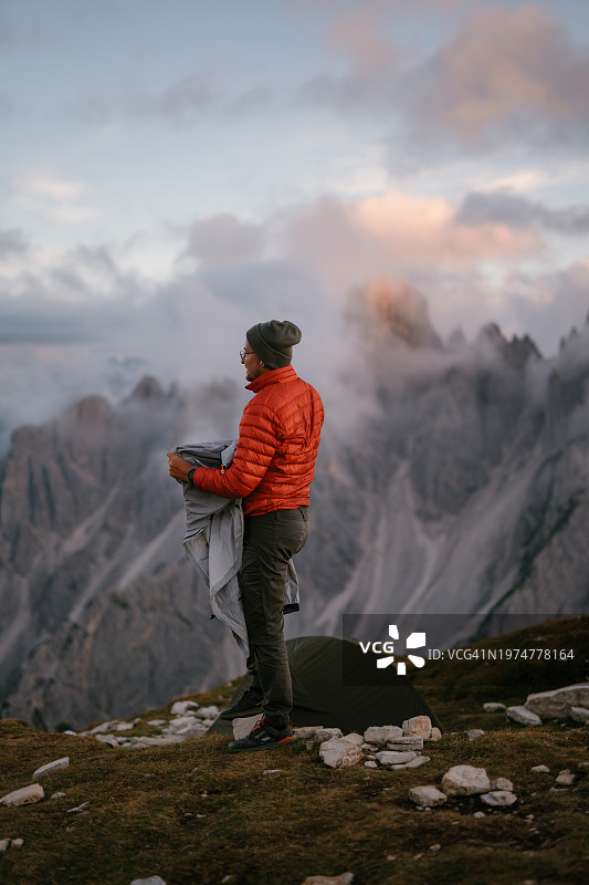 陡峭的悬崖和云层之上的山峰的宁静风景。徒步旅行者站着欣赏风景图片素材