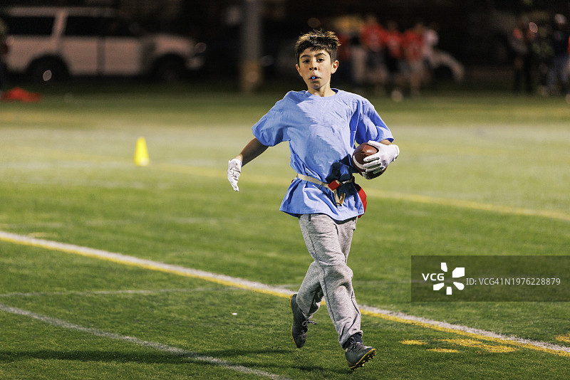 专心致志的男孩拿着美式足球跑过体育场。图片素材
