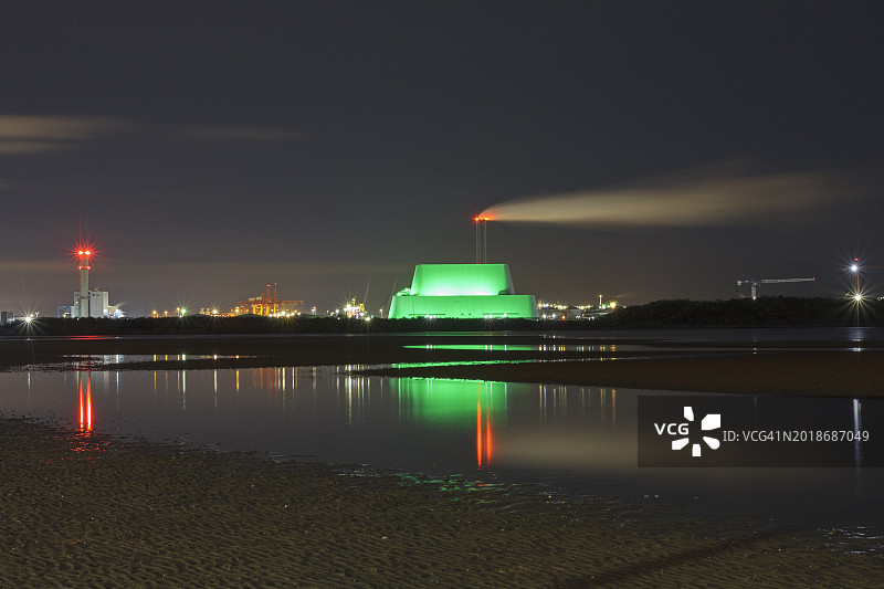 爱尔兰都柏林的焚化炉为圣帕特里克节点亮了绿色。稻田日，世界绿化。废物转化为能源。都柏林港的天际线反映在水从山。图片素材