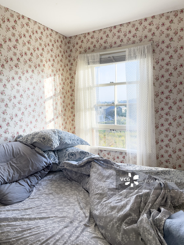 刚睡在床上，在晨光里，小房间里有花墙纸和明亮的窗户图片素材
