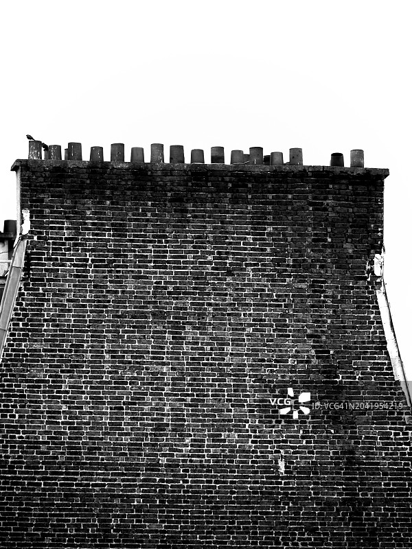 法国巴黎，一座顶部有烟囱的住宅建筑的风化砖山墙特写。黑白照片。阳光。多云的天空。图片素材