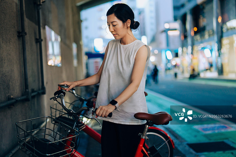 年轻的亚洲女子在城市街道上用智能手机解锁共享单车，用租来的自行车在城市通勤。城市通勤。共享运输服务。可持续生活理念的科技与生活方式图片素材
