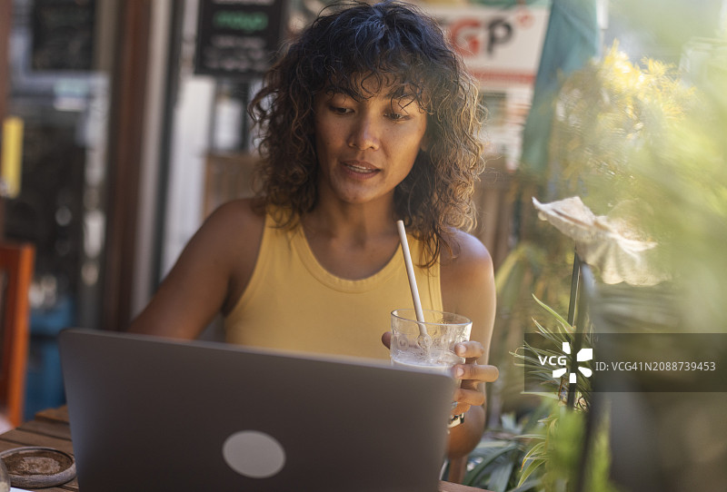一名菲律宾妇女坐在咖啡店里喝着她最喜欢的咖啡，用笔记本电脑进行远程工作图片素材