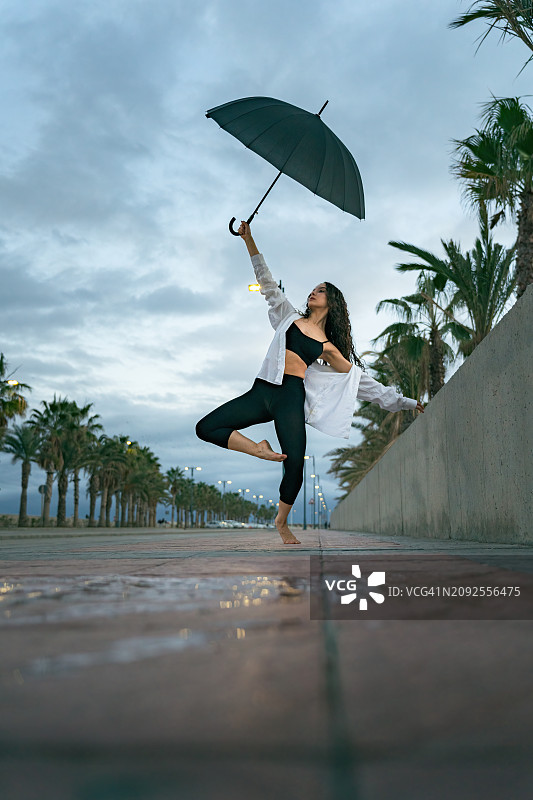 一个赤脚的舞者在下雨天打着伞摆出惊人的舞蹈姿势。图片素材