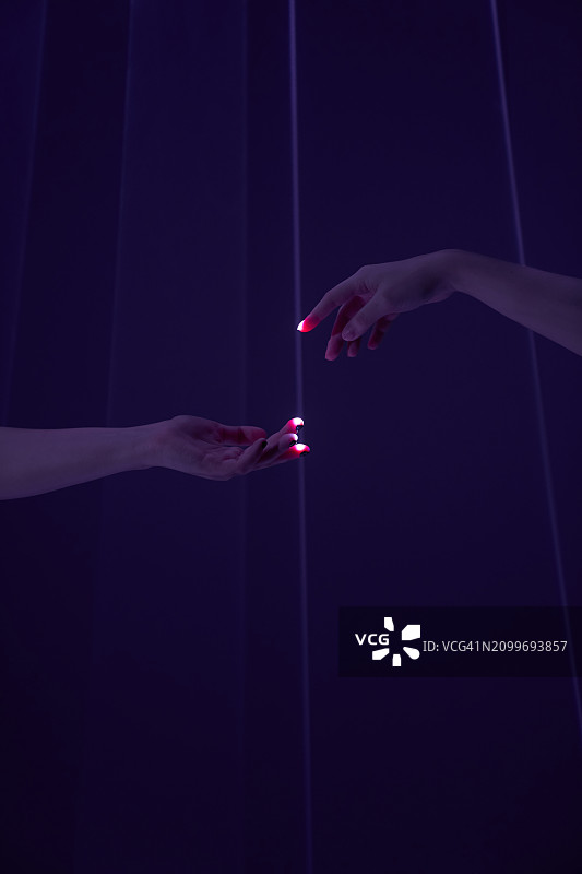 通过紫色背景上的激光束，不同人的两只手相互伸出。在拷贝空间上伸出援手的概念。图片素材