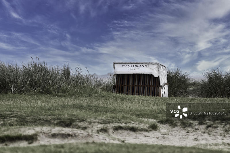 旺格兰沙滩椅，站在沙滩上的旺格兰沙丘上，周围是绿色的草地，背景是明亮的蓝天白云，旺格兰，北海海岸，德国，欧洲图片素材