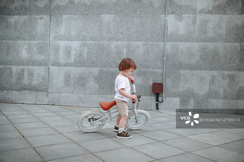 幼儿在城市长廊上测试平衡自行车，在灰色人行道上滚动图片素材