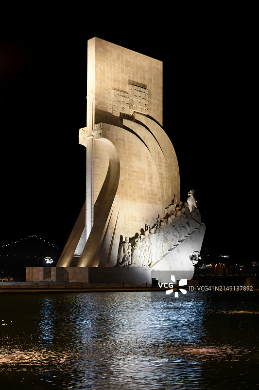 “发现纪念碑”(“Monumento aos Descobrimentos”或“padro dos Descobrimentos”)在夜晚被塔霍河照亮，背景是葡萄牙里斯本的“四月二十五日桥”图片素材