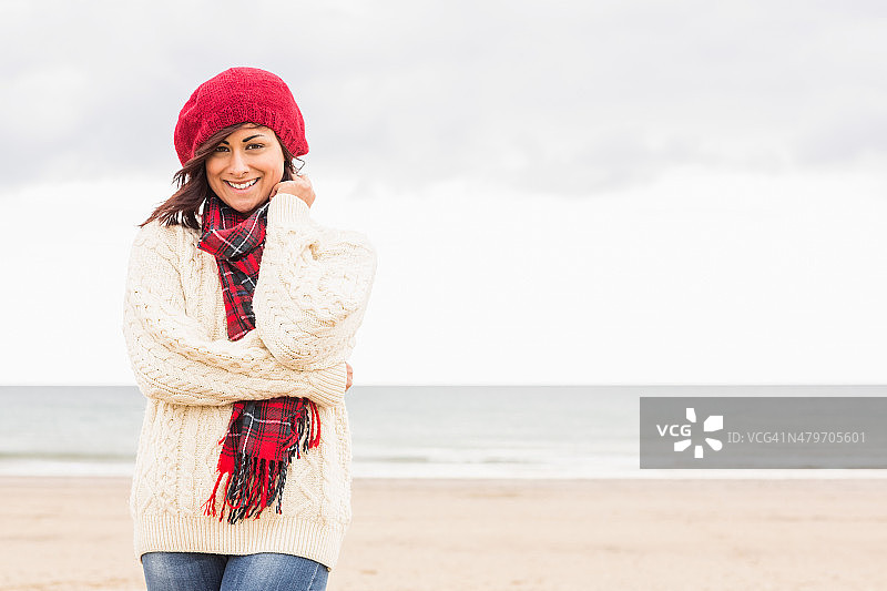 可爱的微笑女人在时尚的温暖的衣服在海滩图片素材